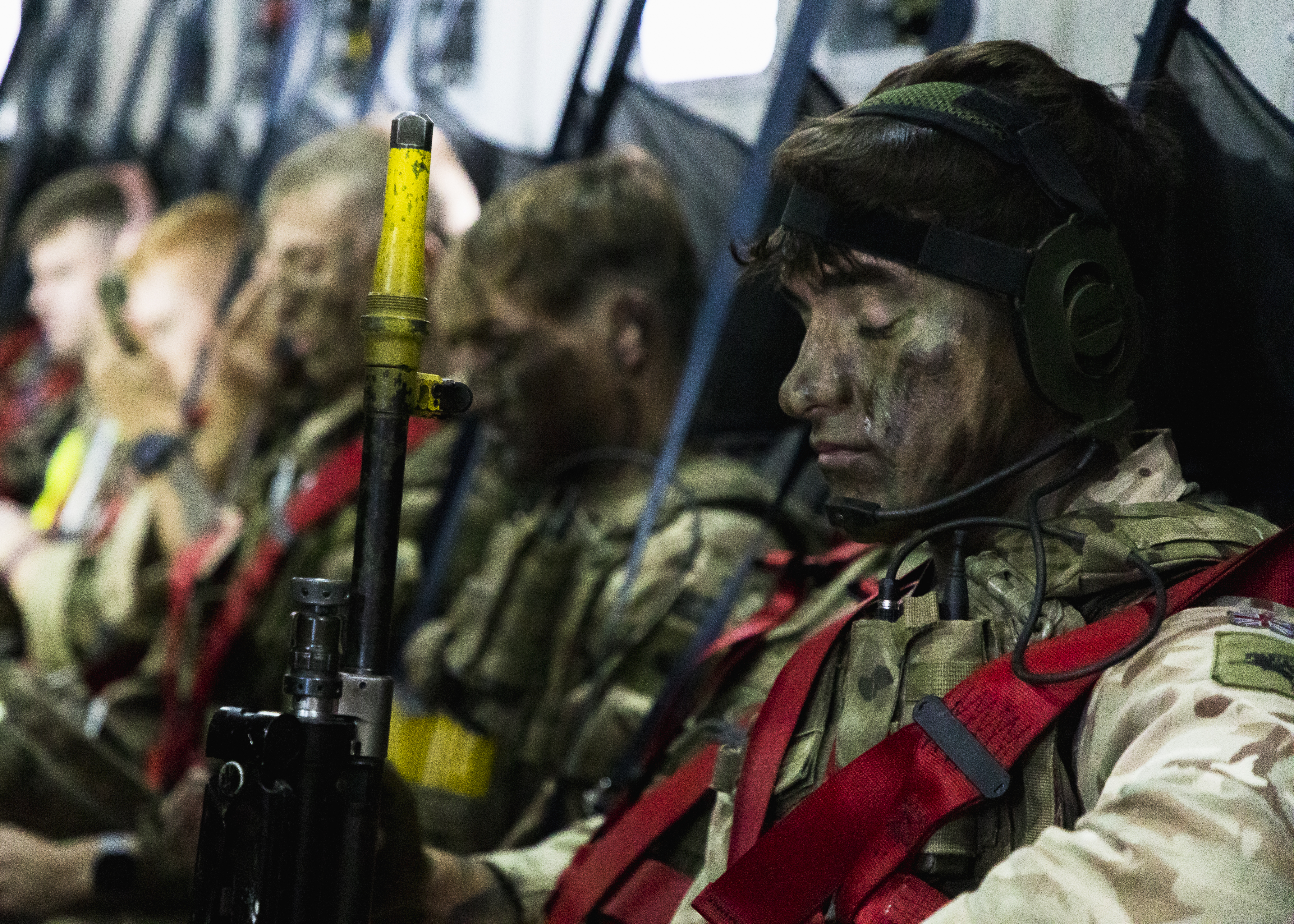 Image shows RAF personnel with face paint and rifles, sitting inside aircraft carrier.